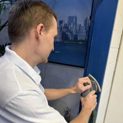 Mann schleift die blaue Tür mit einem elektrischen Schleifgerät ab.